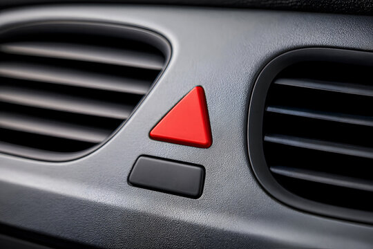 Close-up shot of a red triangle hazard light button and air vents on a modern car dashboard console, representing automotive safety, emergency signal, and interior controls.