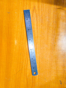 Stainless steel ruler on a wooden workbench table, precision measurement tool for carpentry, drafting, engineering, and school stationery supplies