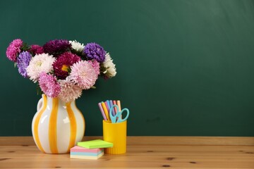 Different stationery and beautiful flowers on wooden table near chalkboard, space for text © New Africa