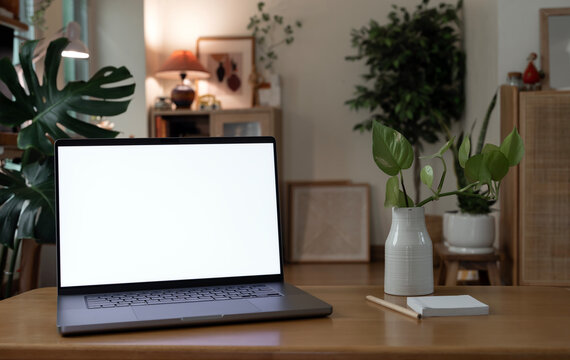 Laptop mockup with blank white screen on wooden desk in cozy room