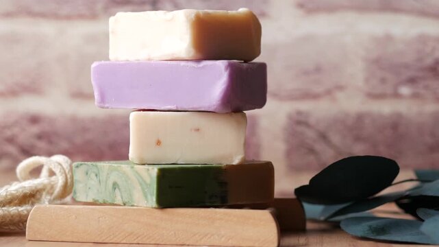 Stack of colorful handmade soaps on wooden stand with natural leaves