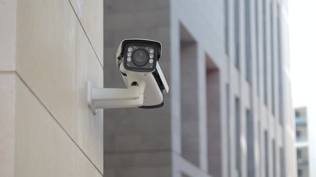 Close up video of modern outdoor security camera on building wall, device slowly rotates and surveils area, technology concept