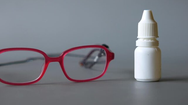 Red eyeglasses and white medicine eye drops bottle on gray background cinematic footage with soft movement and professional lighting
