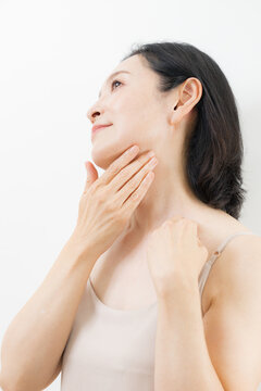 A woman in her 50s caring for her neck and d&eacute;colletage with both hands: A beauty image of middle-aged women practicing anti-aging and skincare