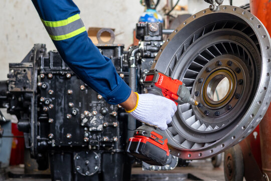 Technician uses cordless impact wrench on torque converter stator inside industrial repair workshop.