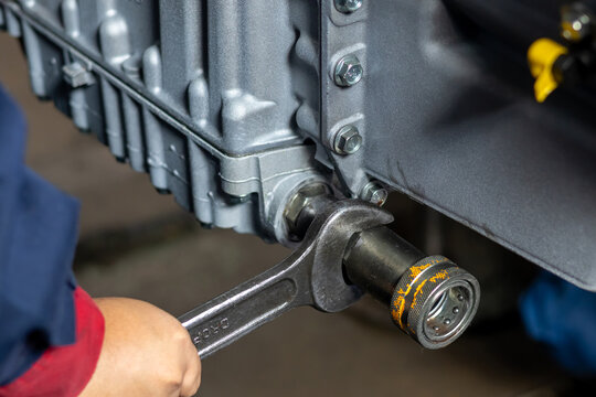 Technician tightens hydraulic quick disconnect coupler with spanner on machinery in workshop.
