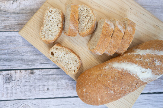 Fresh bread slices rest on a wooden cutting board. Crusty loaf beside slices invites cozy kitchen moments. Light wood table adds rustic charm to simple meal prep