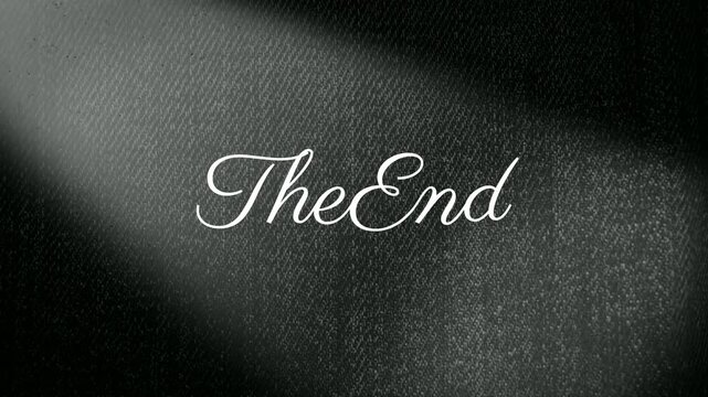 Calligraphy reading the end illuminated by a soft white spotlight against a dark textured fabric background.