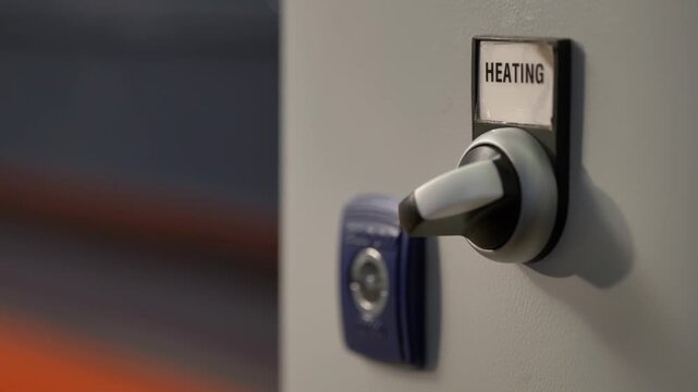 Hand turning heating control switch on industrial machine panel.