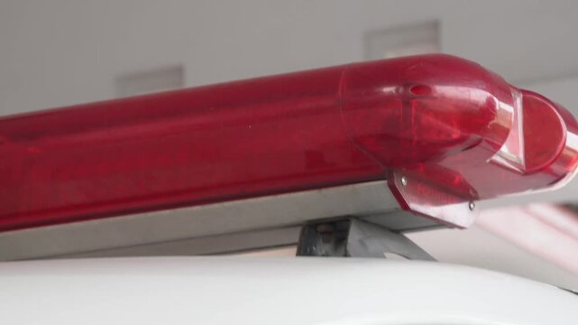Close up view of a red emergency siren lightbar and speaker mounted on the white roof of an ambulance or police vehicle, emergency response equipment, public safety concept, and warning signal device.