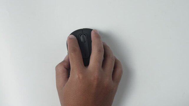 Top view of hand holding and using black wireless computer optical mouse on clean white desk surface, office work, technology, web browsing, and e-commerce clicking concept.