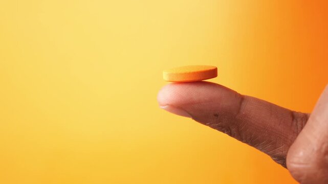 A close up view of person holding orange color medical pill on finger, showcasing health and pharmaceutical concepts