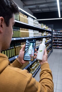 Shopper Holding an Unbranded Oil Bottle and Scanning It with a Phone App That Identifies the Product and Suggests a Cheaper Option