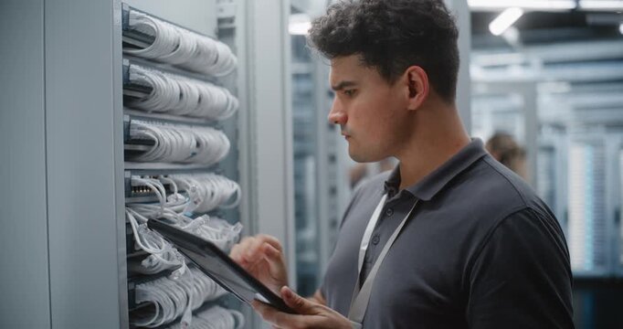 Male Network Technician Audits Patch Panel Connections While Referencing Tablet, Checking Cable Identification and Physical Ports During Digital Verification of Data Center Infrastructure Work.