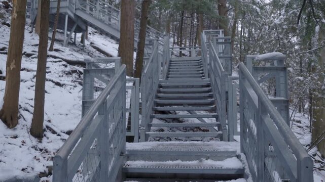 Snow covered metal stairway winding up through forest landscape in winter.