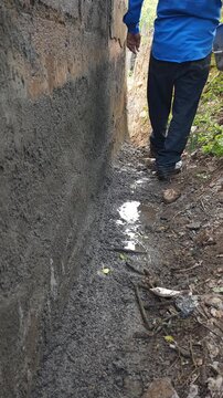 Young Man Carrying Plastic Bucket Walking Along Dirt Path Next to Old Wall