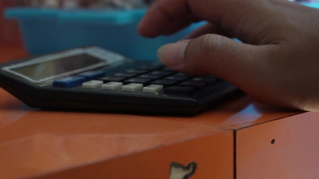 Close up view of hand pressing buttons on electronic desktop calculator placed on orange table, financial accounting concept, budget calculation, business transaction, and office work routine.