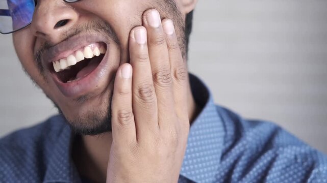 Young man experiencing intense toothache while holding his jaw in pain and suffering from dental problems