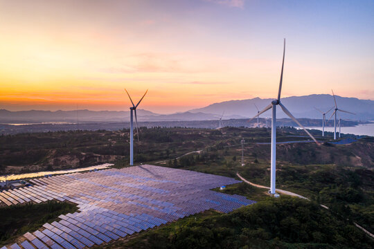 wind turbines and solar panels on hillside at sunset