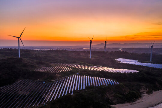 Wind turbines and solar panels on a hillside at sunset