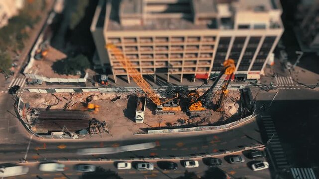 Tilt shift miniature style timelapse of an urban street construction site with heavy equipment digging and busy city traffic flowing nearby