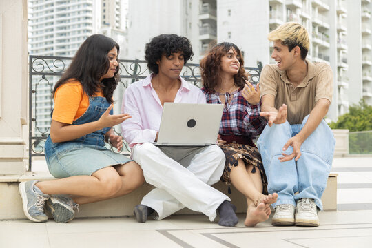 Group of young diverse indian asian students sitting outdoors. engaging in lively discussion while working together on laptop. collaboration and friendship in modern education in india