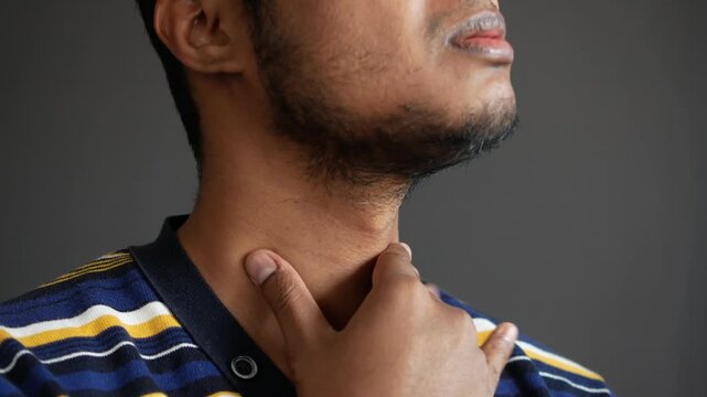 Young man suffering from sore throat and neck pain holding his throat with hand