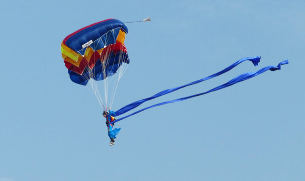 Colorful skydiver with parachute and blue streamers in clear sky