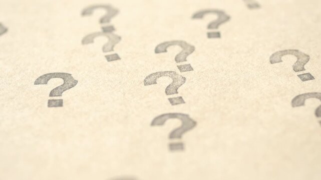Slow motion close up of many question marks printed on paper texture moving across the frame in soft lighting