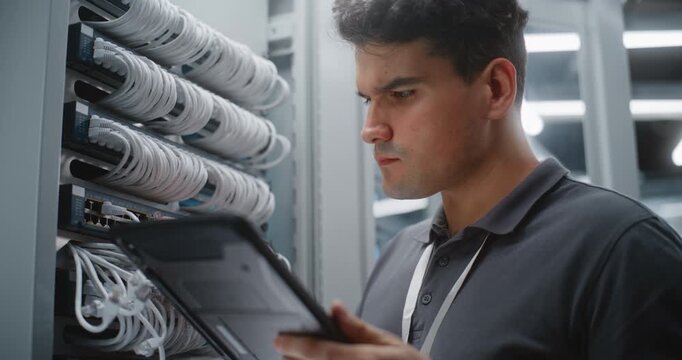 Male IT Engineer Verifies Server Rack Cabling Against Information on Tablet, Inspecting Physical Ports and Cable Labels During Structured Network Infrastructure Audit, Maintenance. Services Equipment.
