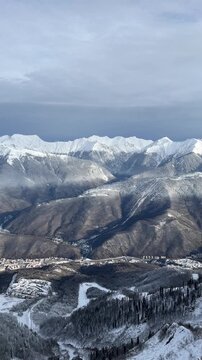 Snow-covered mountains under a cloudy sky. The landscape features rugged peaks and a valley with patches of snow. A serene winter scene.