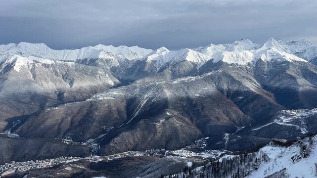 Snow-covered mountains under a cloudy sky. The landscape features rugged peaks and a valley below, showcasing the beauty of winter scenery.