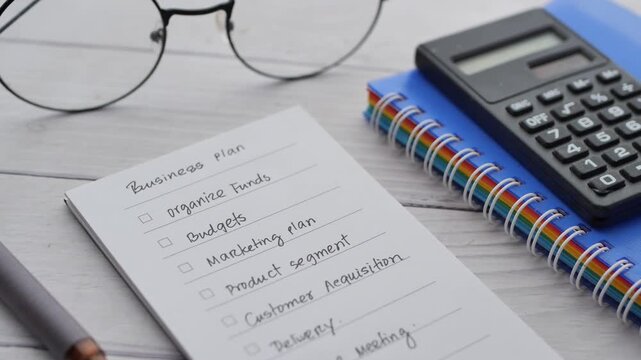 Business plan notes on notepad with calculator and glasses on wooden table accounting and strategy planning concept