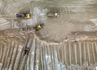 Aerial view of heavy earthmoving equipment and dump trucks working along a sandy shoreline, where machinery is grading and redistributing sand near the water’s edge.  © PixilRay
