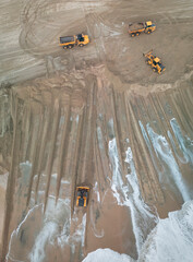 Aerial view of heavy earthmoving equipment and dump trucks working along a sandy shoreline, where machinery is grading and redistributing sand near the water’s edge.  © PixilRay