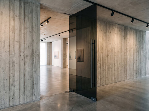 Modern minimalist art gallery interior with concrete walls, glass sliding door, and polished concrete floor with contemporary artwork display