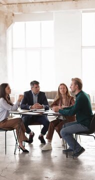 Diverse group of corporate employees sitting at table analyzing paperwork planning startup strategy brainstorming insights collaborating on business ideas during inclusive discussion. Vertical video