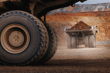Closeup of giant haul truck wheels with loaded dump truck in dusty open pit for industrial background © Parilov