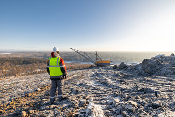 Worker observing excavator in snow covered landscape, open pit mine coal. Industry mining concept