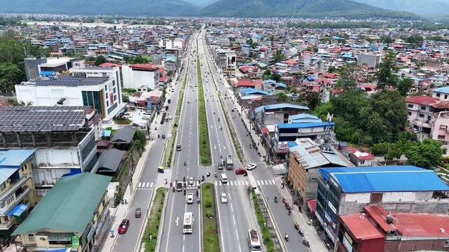 High angle aerial view of a major divided highway with pedestrian crossings leading into a sprawling metropolitan basin in Nepal