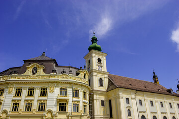 Obraz premium The historic Sibiu Lutheran Cathedral and the Brukenthal National Museum in Romania under a clear blue sky.