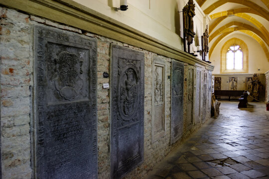 Interior view of a church hallway with stone sarcophagi and a stained glass window.