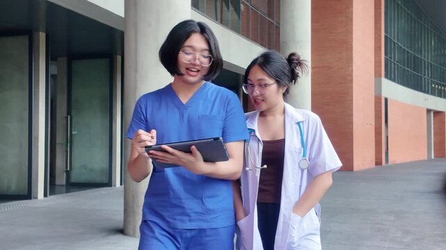 Young medical students in scrubs and lab coat walking and reviewing data on digital tablet, medical university students walking together while discussing notes on a tablet computer outdoors