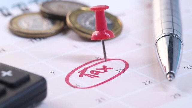 Slow motion close up of calendar with tax day marked by red pin and circled date next to pen and coins