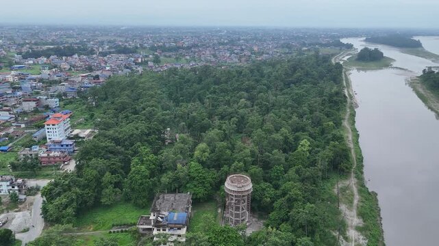 Aerial perspective of a dense green forest park featuring an observation water tower separating a vibrant city from a wide muddy river