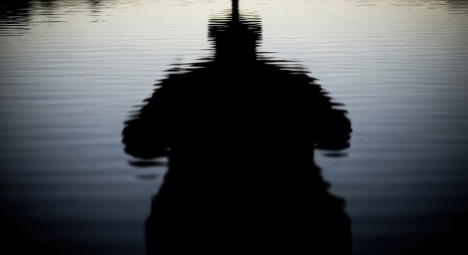 Silhouette of a Person Fishing in Calm Waters at Dusk.