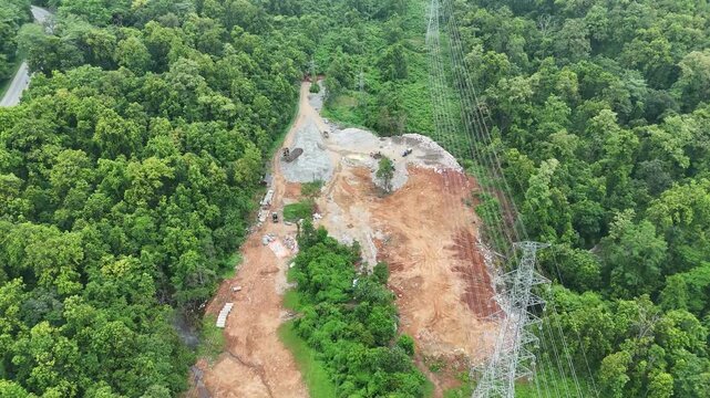 Aerial landscape of a deforested landfill waste site operating directly beneath a major electrical transmission corridor in a dense jungle