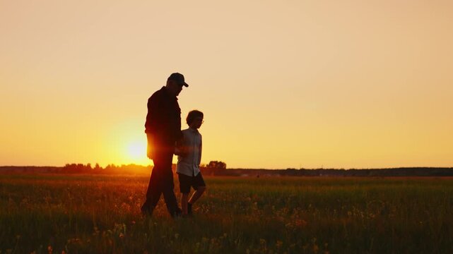 Silhouette of father and son walking together through peaceful meadow at golden sunset, sharing quiet bonding time in nature under warm glowing evening sky