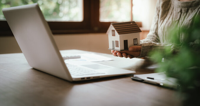 Real estate professional holding a model house at a desk with property documents, representing home ownership, mortgage, investment, and property transactions.