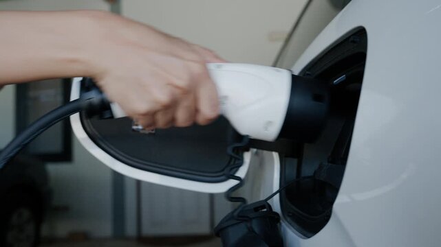 Person plugging off EV charging cable to white electric vehicle for sustainable energy transport.	